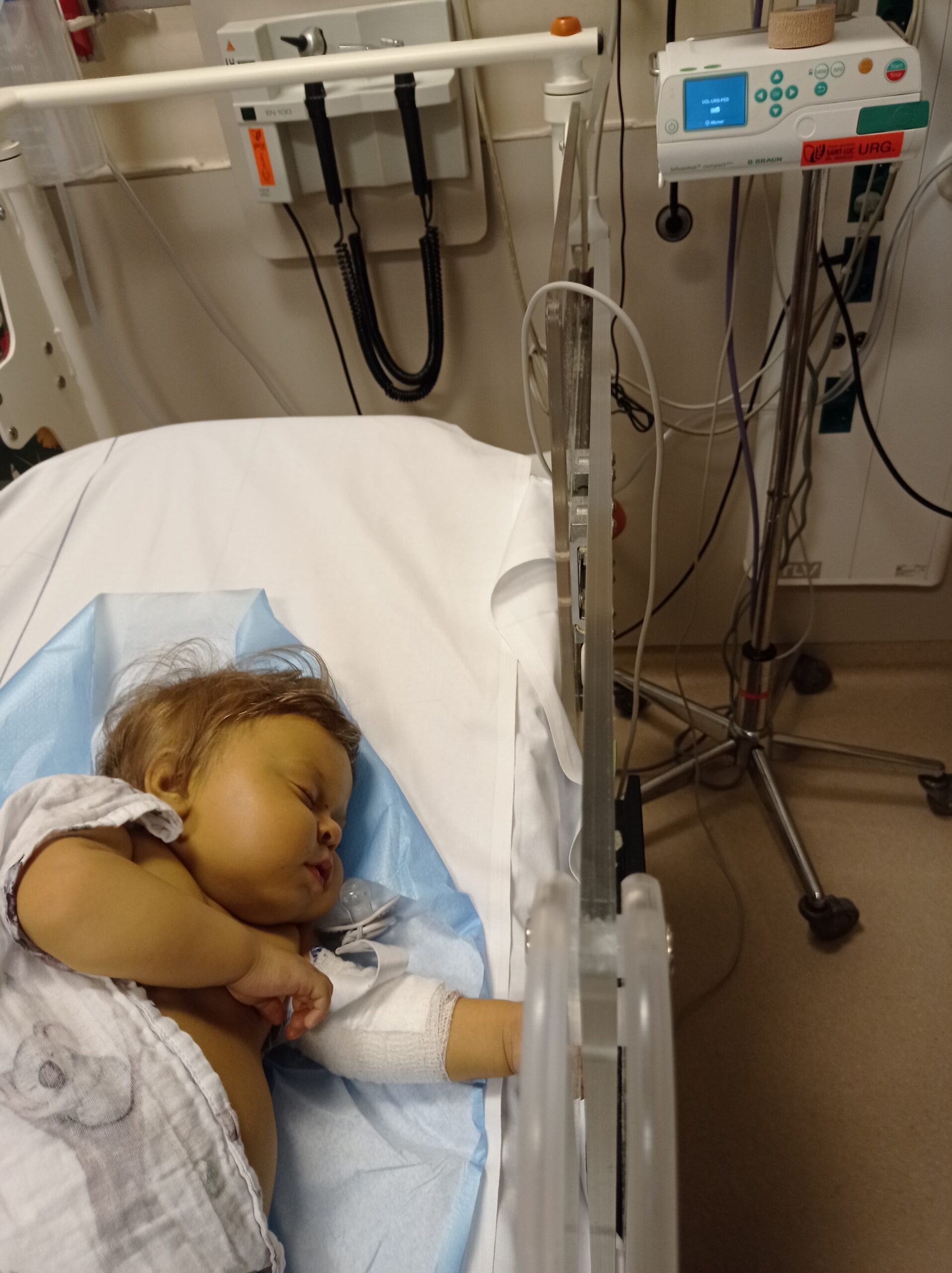Łóżko szpitalne i podpięta do aparatury leżąca w nim mała śpiąca dziewczynka